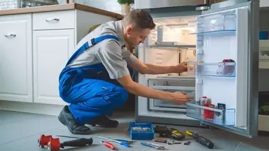 Technician examining a compact refrigerator with service tools nearby