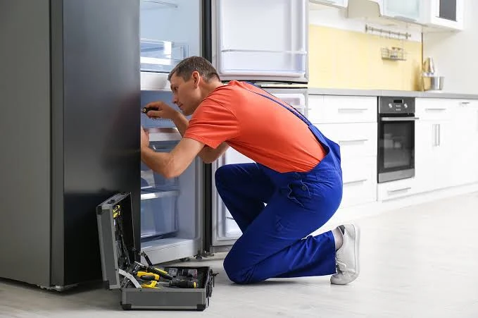 Technician checking the interior of a refrigerator with a tool case nearby